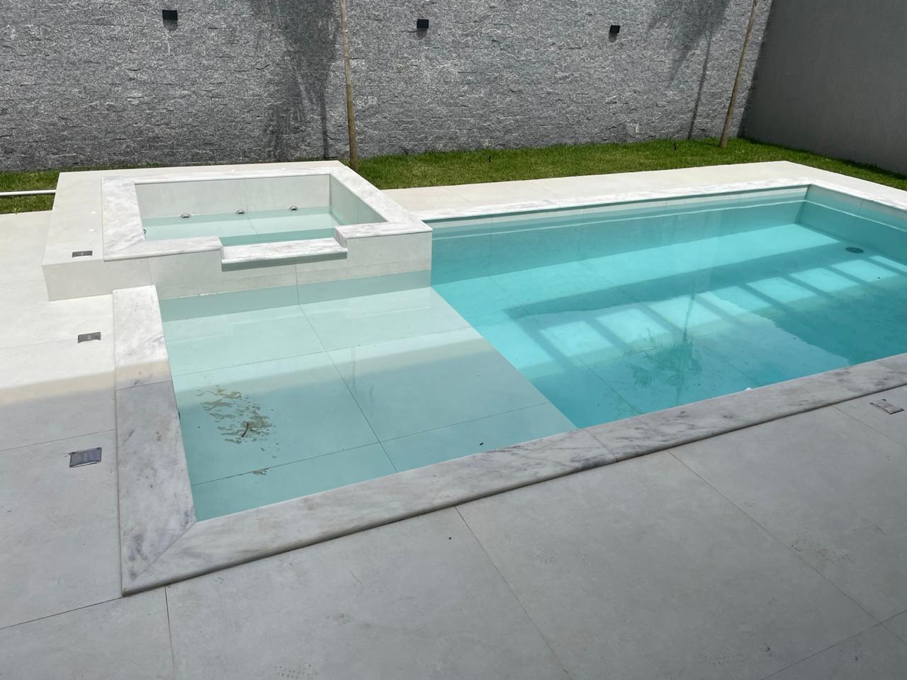Área de lazer residencial com piscina, spa e revestimentos claros